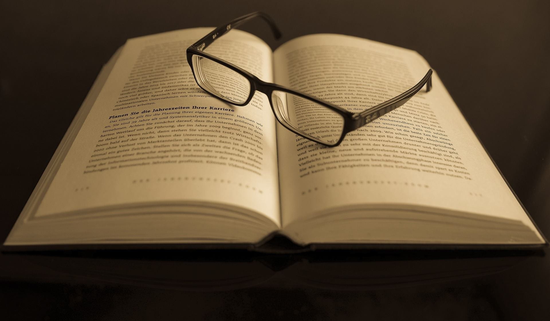 A picture of glasses resting on an open page of a text based book.